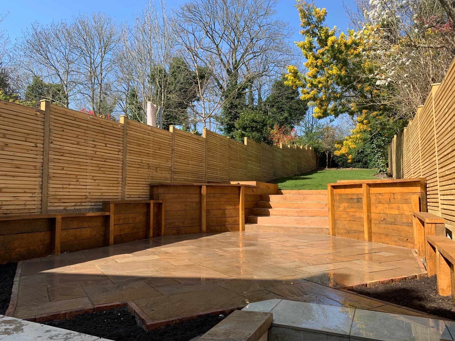 Sunken sandstone patio with hardwood sleeper retaining walls and herringbone brick steps